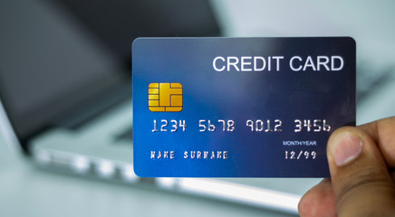 Close up holding a blue credit card placed in front of the laptop. online shopping payment and...