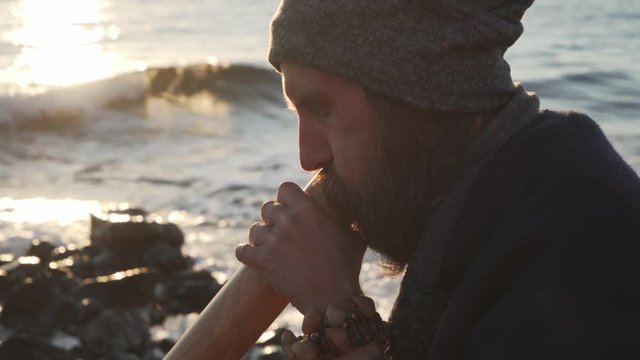 Close up man's hands playing a didgeridoo in sunshine at seashore