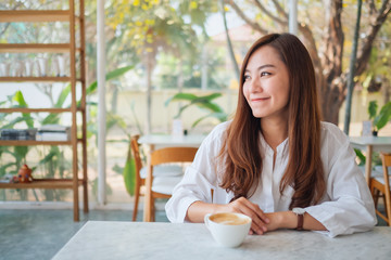 Closeup image of a beautiful asian woman sitting in cafe with coffee cup on the table