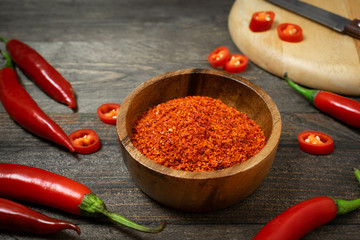 Cayenne in small bowl with chili on wooden table.