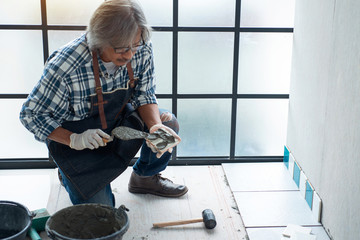 Asian senior man while using spacer for installing tiles, tiled technicians are tiled ceramic for...