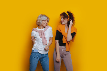 Two joyful casucasian women with curly hair are listening to music through headphones on a yellow headphones - Powered by Adobe