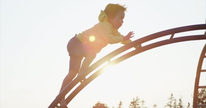 Young boy climbing play structure at sunset in spring - look of dedication on his face