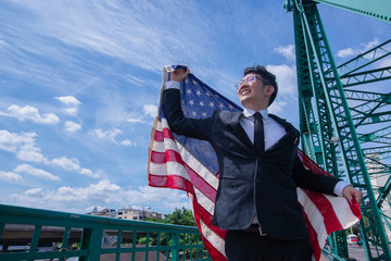 Asian business man in suit raise hands up and waving American flag for his success.agains cloudy blue sky, concept of success, Independence day concept, 4th July