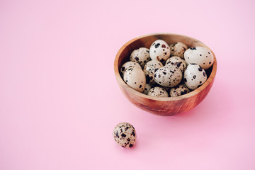 Quail eggs in wooden bowl on a pink background. Easter concept, flay lay photo. Mockup, space for text.