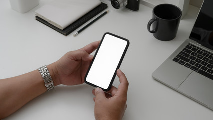 Fototapeta na wymiar Cropped shot of male holding blank screen smartphone on white desk