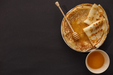 Delicious homemade pancakes with honey on a black background. Top view, close-up. Traditional holiday celebration concept. Russian translation wide and happy Shrovetide Maslenitsa.
