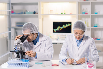 Busy multi-ethnic laboratory researchers in safety goggles sitting at desk and working with samples