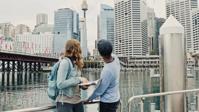Slow motion shot of multiracial couple pointing out and admiring Sydney's landmarks from the pier at Darling Harbour. 
