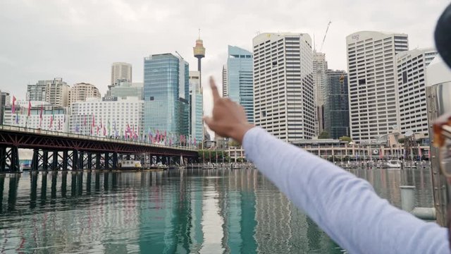 Zoom into a tourist couple pointing out Sydney landmarks from Darling Harbour wharf, followed by a zoom out to reveal the city skyline