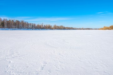 A large frozen river covered with even snow. Clear sunny day