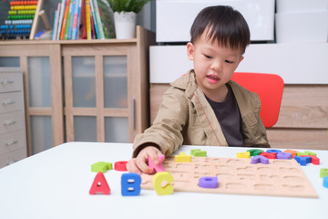Cute smiling kindergarten boy playing with alphabet blocks, Asian children learning English with wooden educational abc toy puzzle for kids, Teach young kids English at home concept