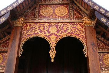 Decoration on gable of Thai dark brown wood church in northern style, native design of golden line on dark brown wood pediment.