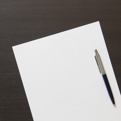 Template of white paper with pen on dark wenge color wooden background.