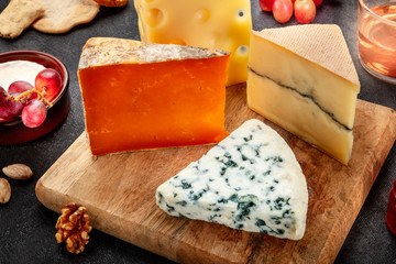 Cheese plate. Blue cheese, red Leicester, goat cheese, and Emmental, on a wooden platter with grapes