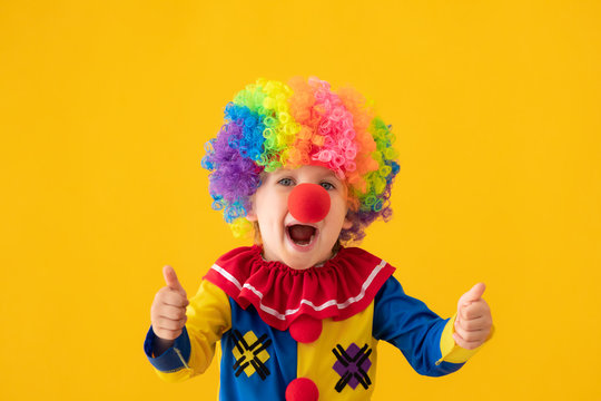Funny kid clown playing against yellow background