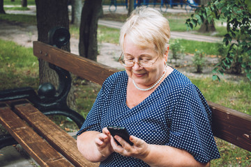 Cheerful old woman with smartphone at park. Outdoor portrait of happy senior woman at park using...