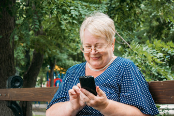 Cheerful old woman with smartphone at park. Outdoor portrait of happy senior woman at park using mobile phone. Plus size blond elderly woman have video call