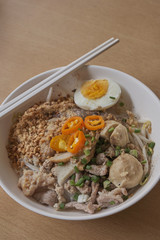 Rice noodles tom yum with pork,fish ball in white bowl on the table; spicy thai noodled.