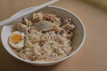 Rice noodles tom yum with pork,fish ball in white bowl on the table; spicy thai noodled.