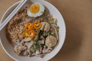 Rice noodles tom yum with pork,fish ball in white bowl on the table; spicy thai noodled.