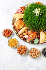 Novruz Azerbaijan traditional table setting, delicious sweet pastry on light background with green wheat grass semeni. Golden plate of pakhlava and shekerbura and gogal, copy space