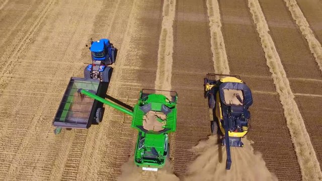 Amazing aerial drone view on modern new huge industrial combiner trucks machines harvesting crops on sunset wheat field