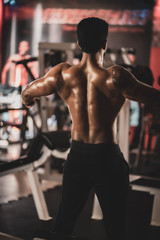 Fototapeta na wymiar Muscular bodybuilder guy standing on gym and posing abdominal muscle
