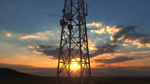 Flying up close to telecommunication tower against scenic sunset. Telecommunications cellular towers providing high speed 4g and modern ultra high speed 5g network service covering large terrain areas