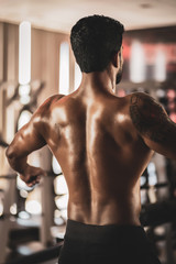 Muscular bodybuilder guy standing on gym and posing abdominal muscle