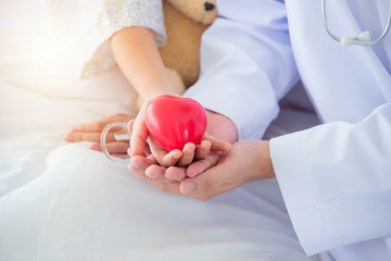 Hands of child patient and male doctor holding red heart shape ball,Organ donation concept.