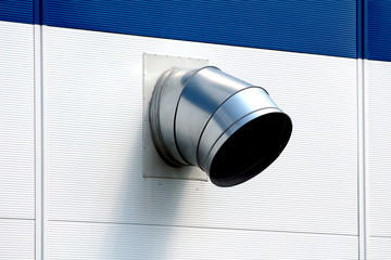 Curved large diameter metal pipe ventilation exit mounted on side of new industrial building wall...