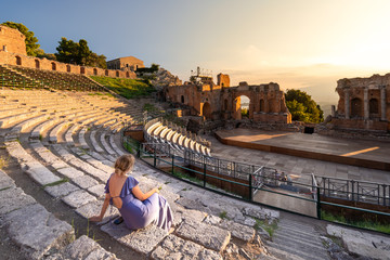 A woman dressed in purple beholds a dramatic sunset at the Greek Theater in Taormina, Sicily