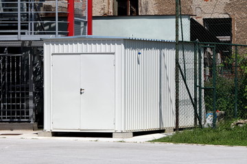 New shipping container converted into storage area with metal locked doors in front mounted on concrete foundation surrounded with wire fence and outdoor stairs metal construction at high school backy