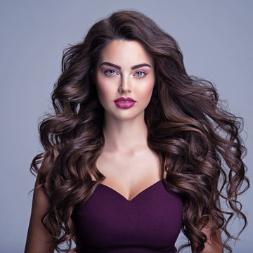 Face of a beautiful woman with long brown curly hair. Fashion model with wavy hairstyle. Attractive young  girl with curly hair posing at studio. Female face with purple makeup. Violet make-up.