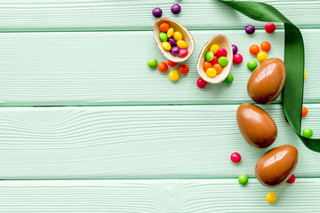 Easter background with chocolate eggs and dragees on green wooden background top-down frame copy space