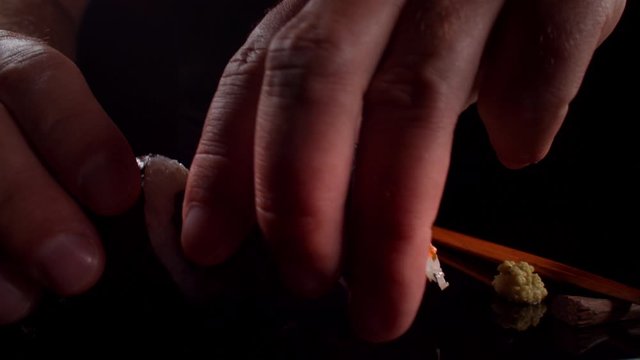 Sushi being served in a dark minimalist studio scene with hands and chopsticks, professionally lit and shot with macro wide angle. slow motion