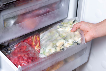 Freezer and frozen vegetables, a person taking food from the freezer - obrazy, fototapety, plakaty