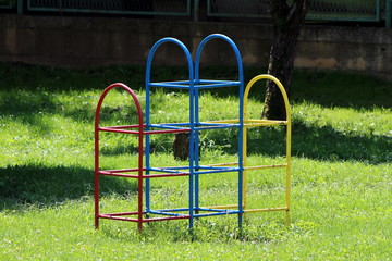 Partially rusted colorful climbing retro vintage outdoor public playground equipment surrounded with uncut grass trees in local public park