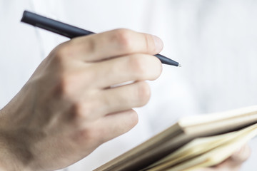 Man writes standing with a pen in notepad in a sunny office, business and education concept. Close up