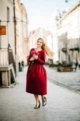 Fashion portrait of young stylish lady woman with bouquet of flowers walking on the street, wearing cute trendy outfit, beautiful girl in a red dress smiling enjoy her weekends.