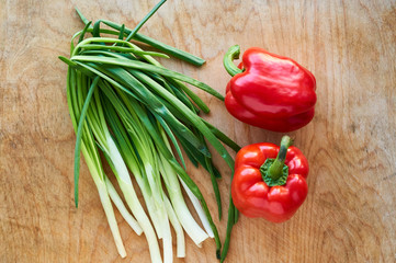 Green onions and red bell pepper on old wooden background