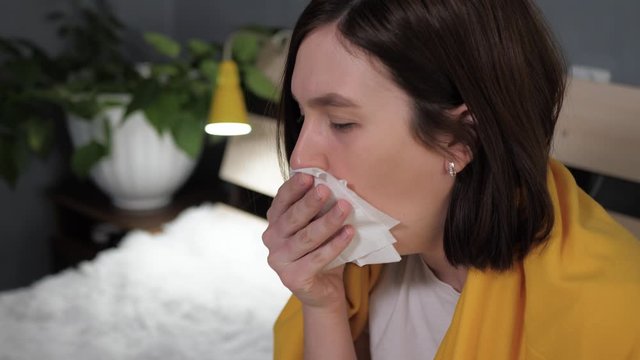 Girl coughs. Attractive young woman coughs intensively and covers her mouth with napkin. Cold, flu, sore throat, acute respiratory disease concept. Slow motion close up