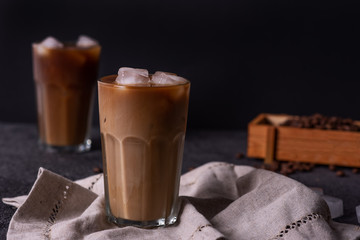 Iced coffee in a tall glass with cream poured over. Wood background. Low key.