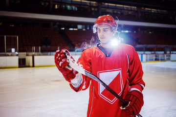 Attractive caucasian hockey player standing on ice and removing ice from stick. Hall interior. Winter sports. © Dusan Petkovic