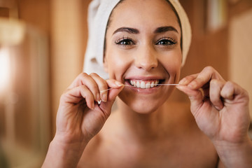 Beautiful woman using dental floss and cleaning her teeth in the bathroom.