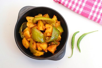 Dry capsicum and potatoes curry. also known as Aloo shimla mirchi Masala. served in black bowl with chilies and coriander over white background with copy space.