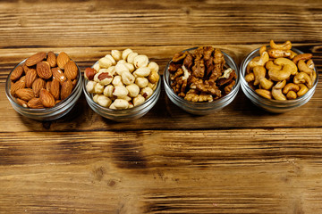 Assortment of nuts on wooden table. Almond, hazelnut, walnut and cashew in glass bowls. Healthy eating concept