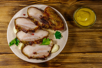 Baked pork belly in a plate on wooden table. Top view
