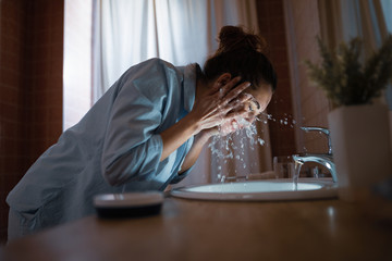 Young woman washing face with water in the bathroom. - obrazy, fototapety, plakaty